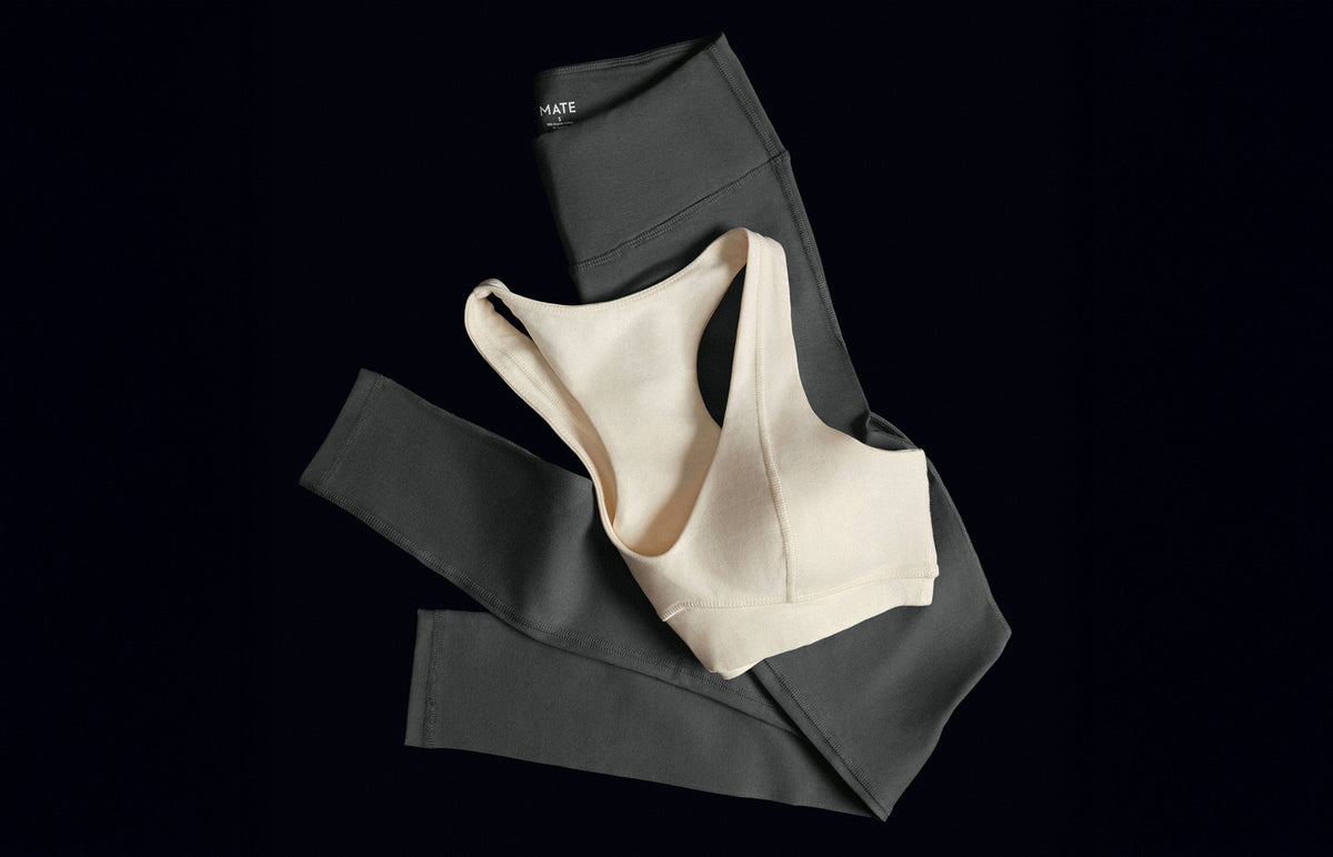 Cream organic stretch sports bra and charcoal leggings set laid flat on black – MATE the Label