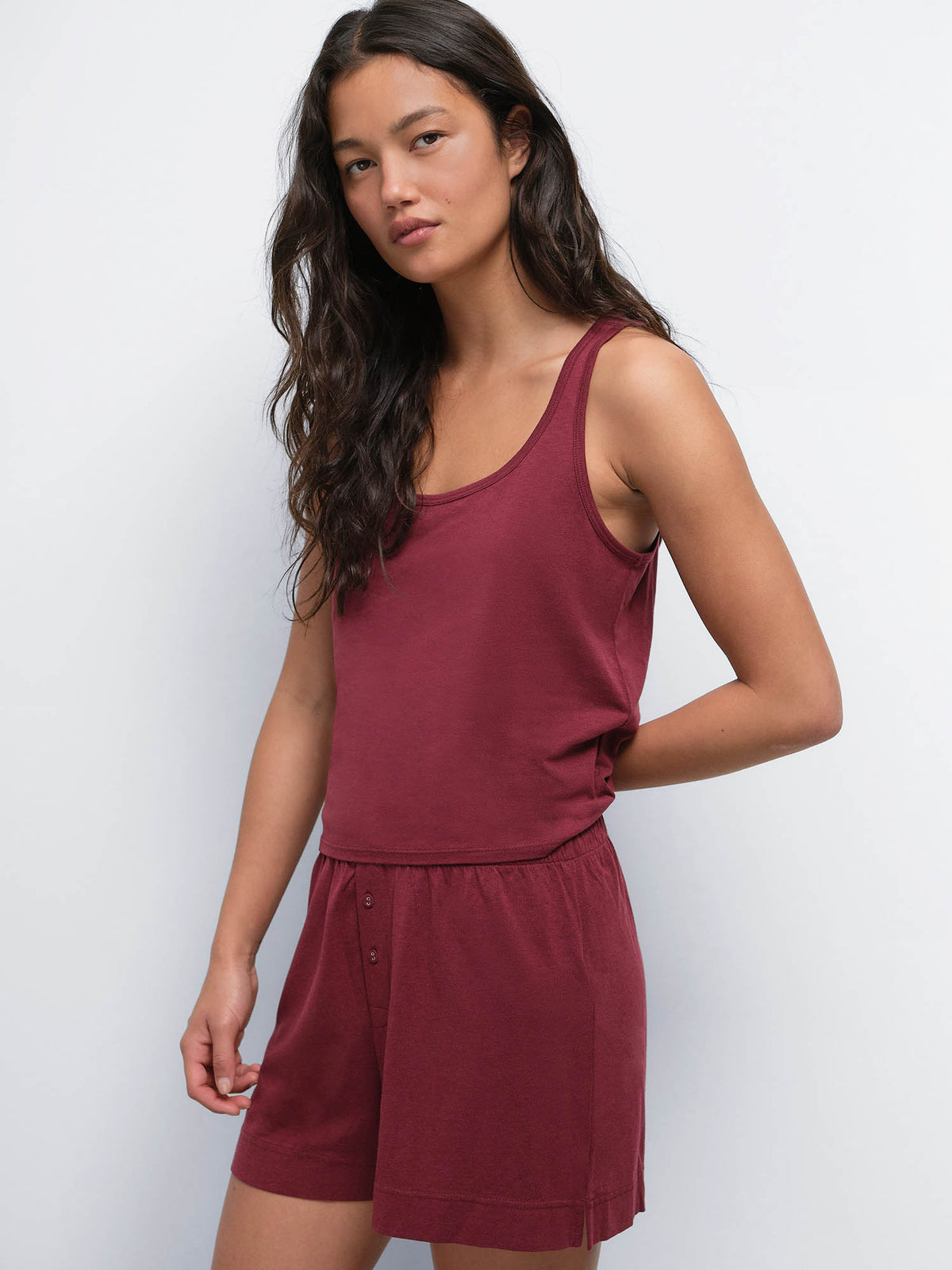 Model with hand behind her back wearing the Tencel Sleep Scoop Tank in Garnet with matching shorts