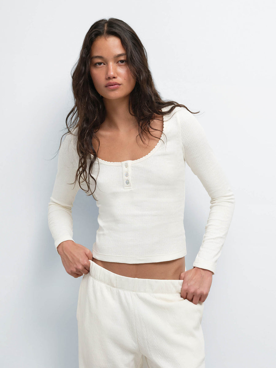 Model with hands in pockets wearing the cropped Organic Pointelle Henley and Jogger in Cream