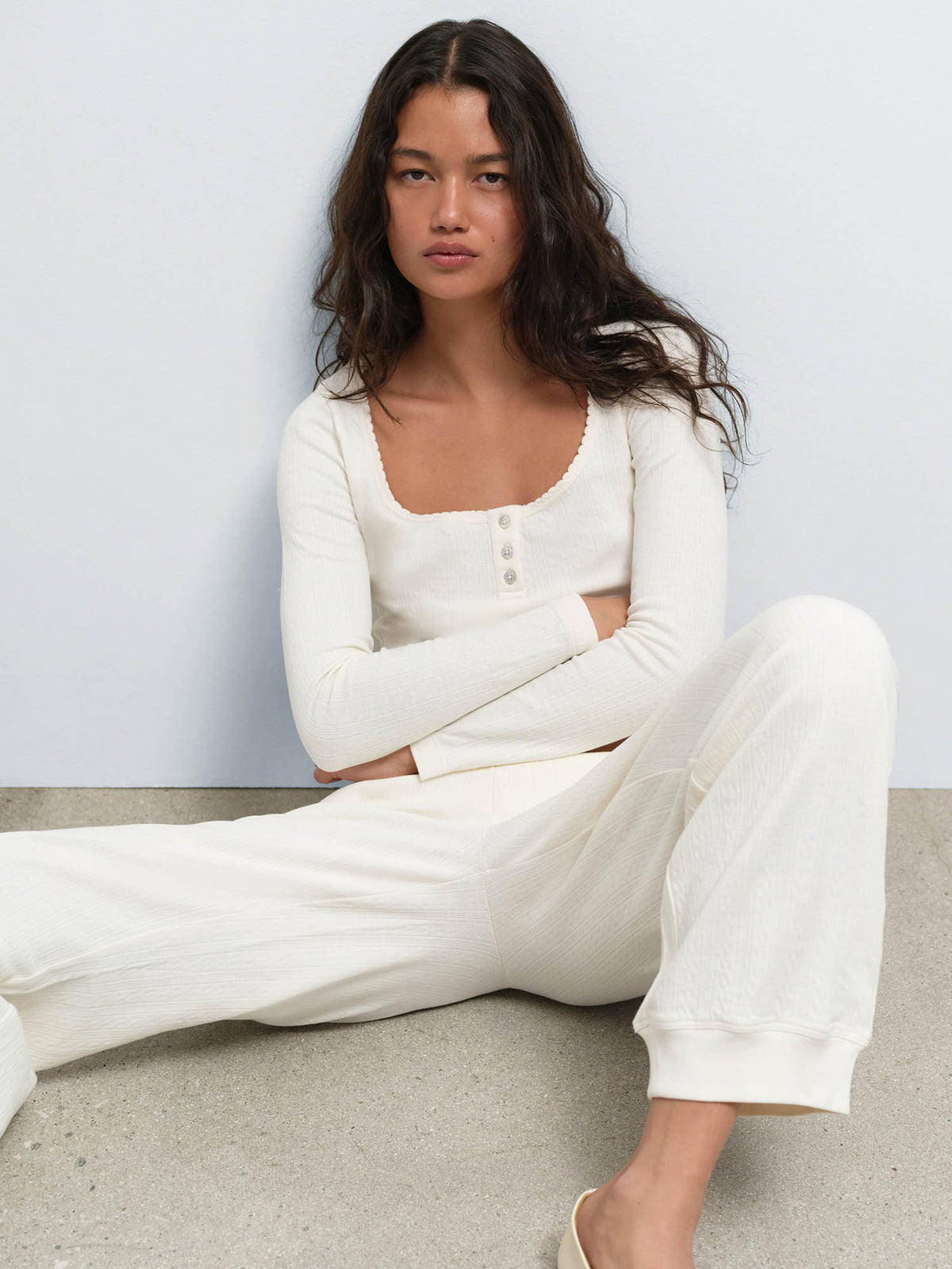 Model seated on the floor wearing the Organic Pointelle Henley and Jogger in Cream
