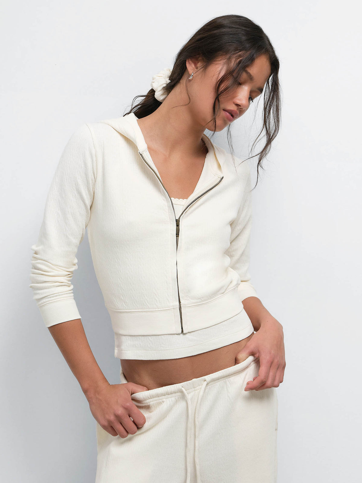 Model looking down and adjusting the waistband of the Organic Pointelle Pant in Cream, wearing the matching Shrunken Hoodie