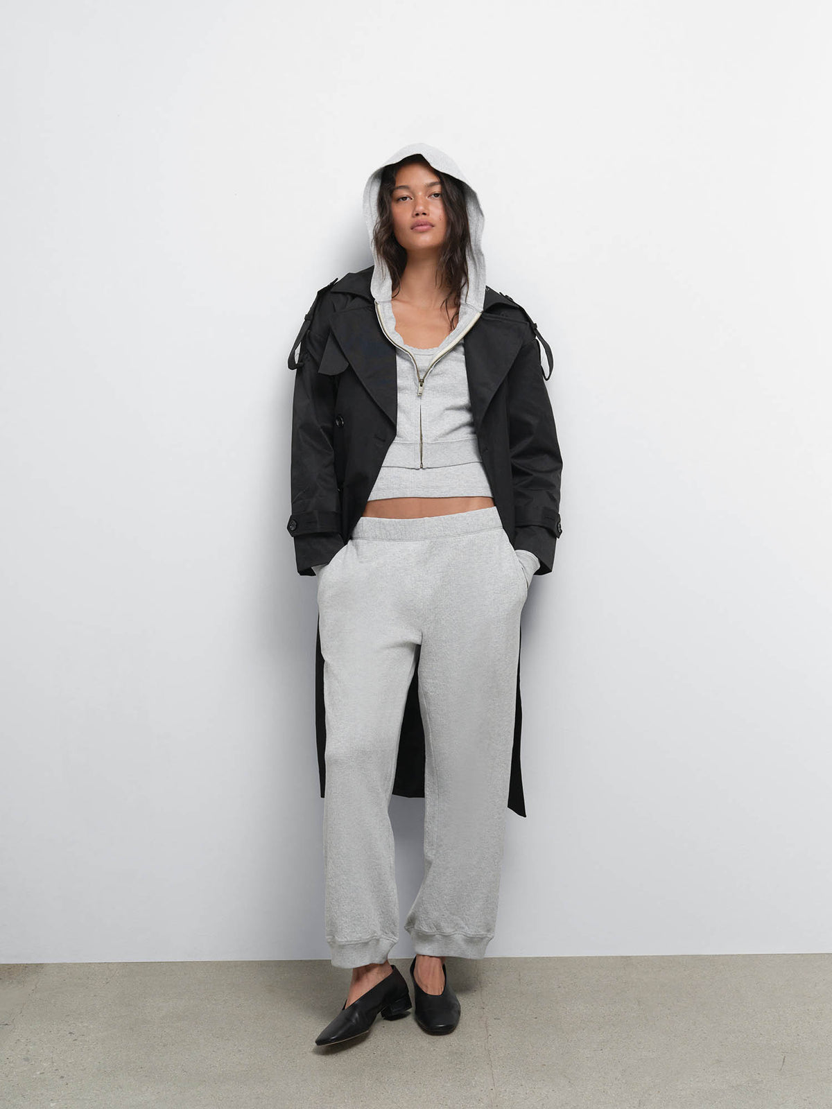 Full-length view of model in a black jacket over the Organic Pointelle Shrunken Hoodie and Jogger in Heather Grey