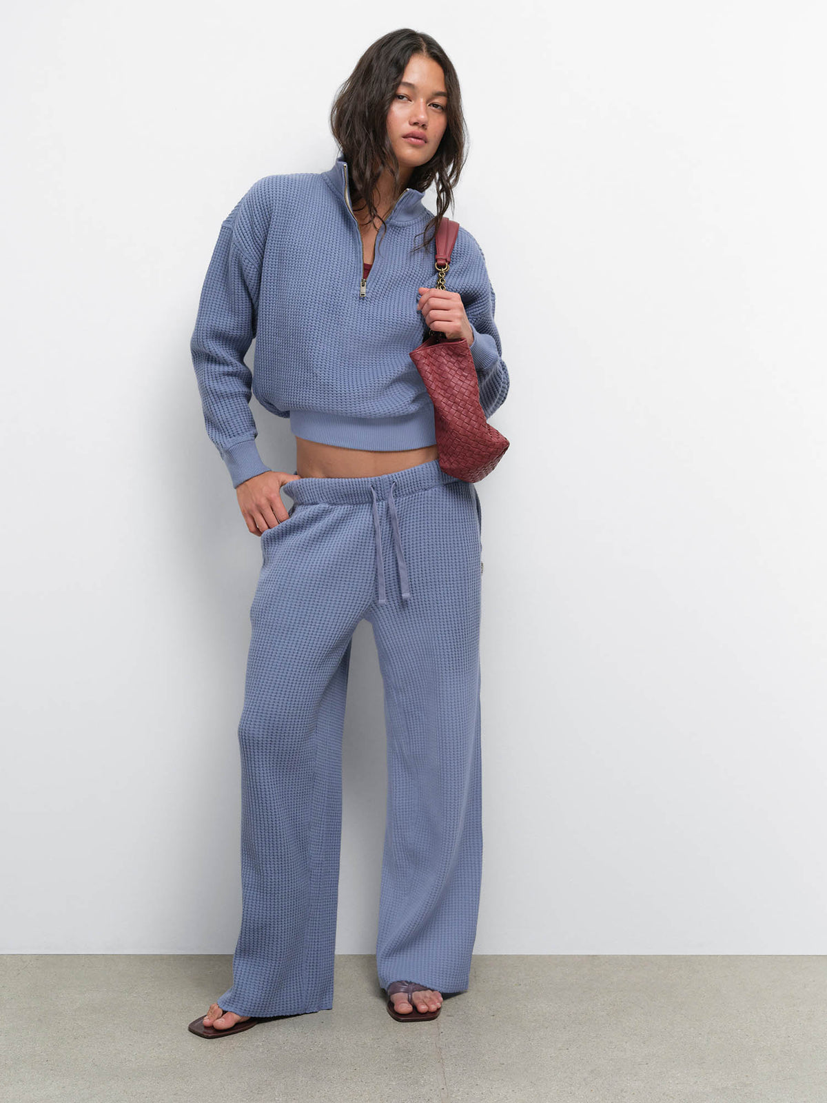 Model holding a red bag wearing the Organic Waffle Collared Half-Zip and Straight Leg Pant in Bay