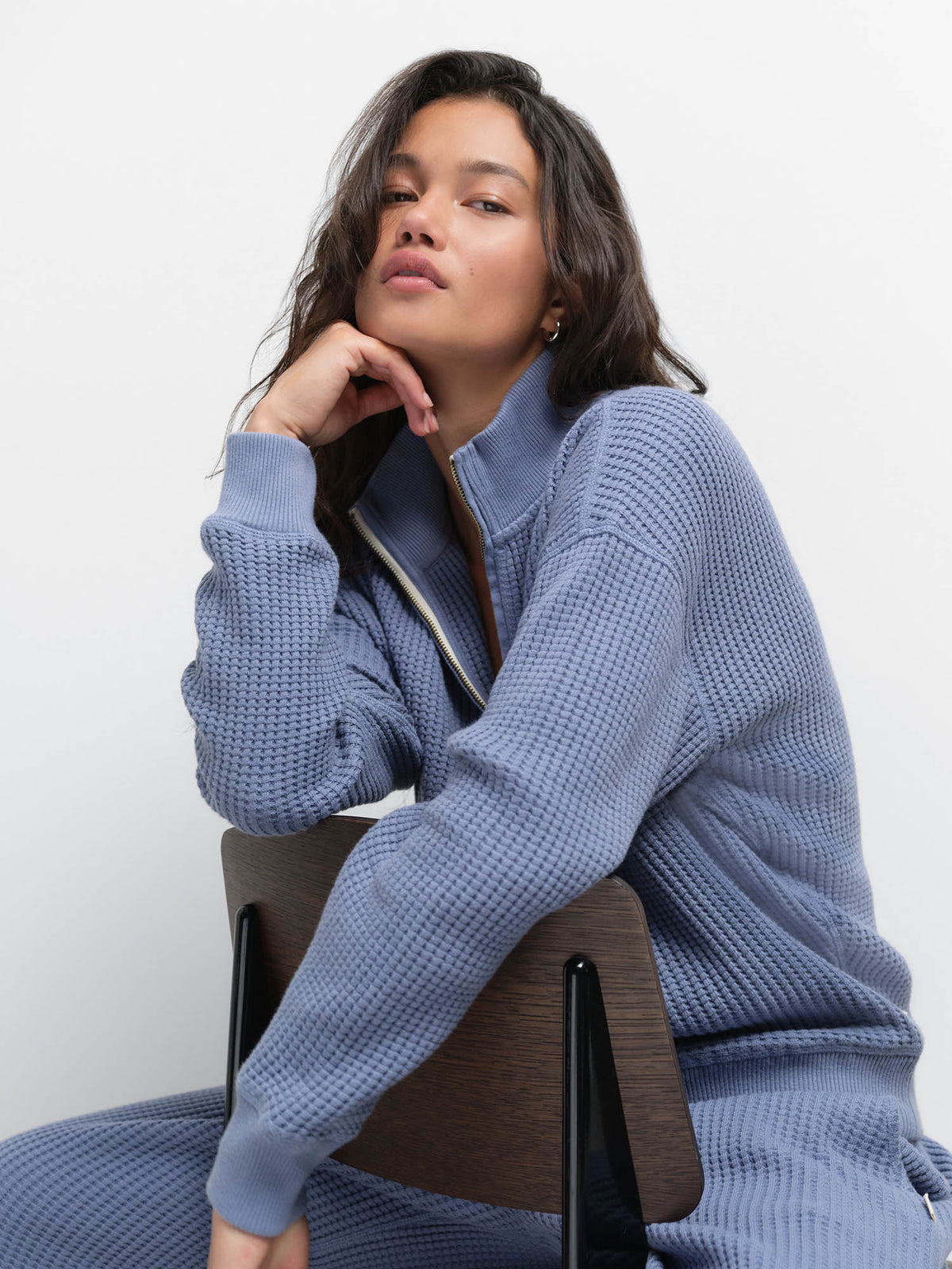 Seated model resting her chin on her hand, wearing the Organic Waffle Collared Half-Zip in Bay