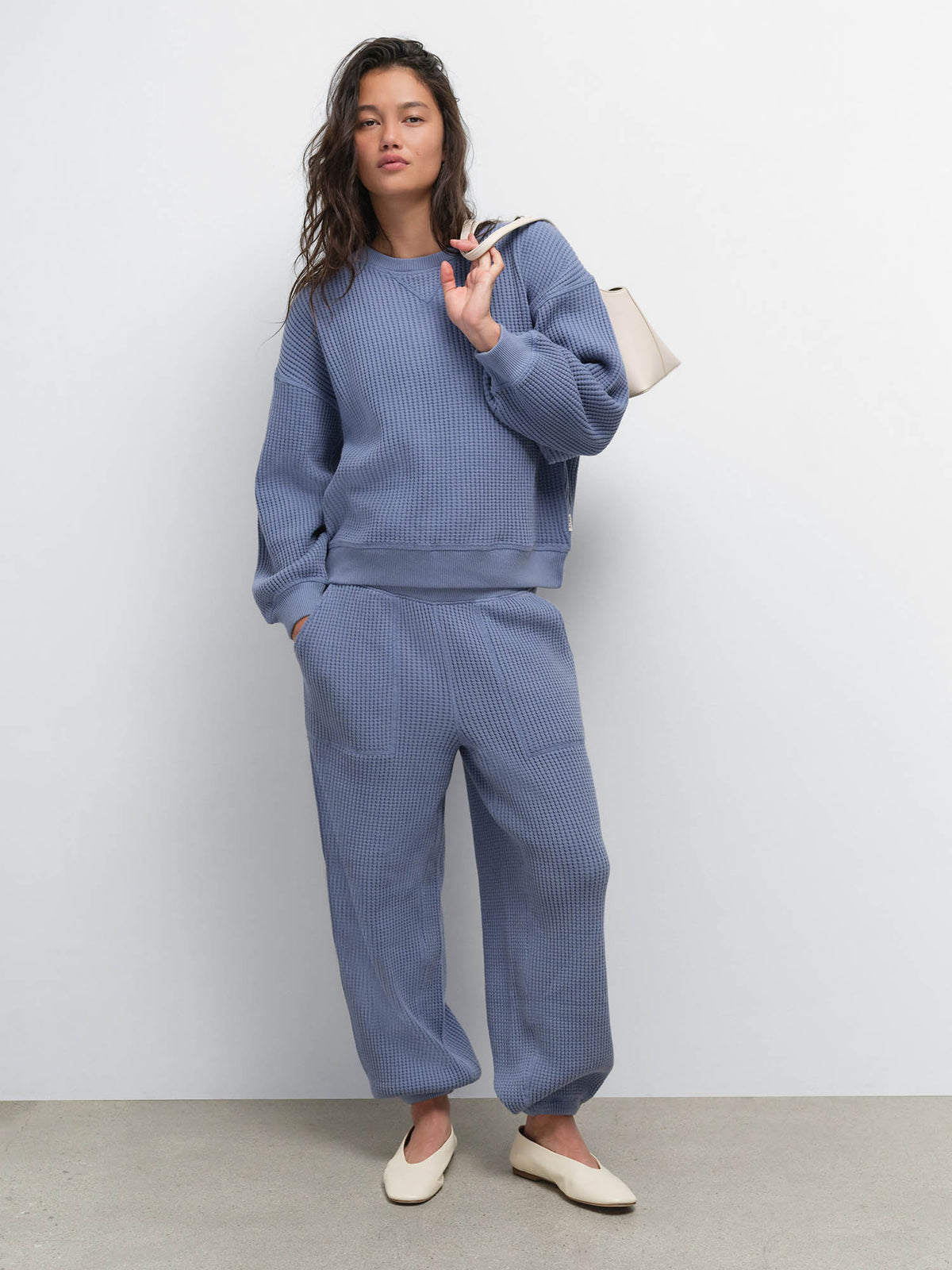 Full-length view of model with a shoulder bag wearing the Organic Waffle Crewneck Sweatshirt and Sweatpant in Bay