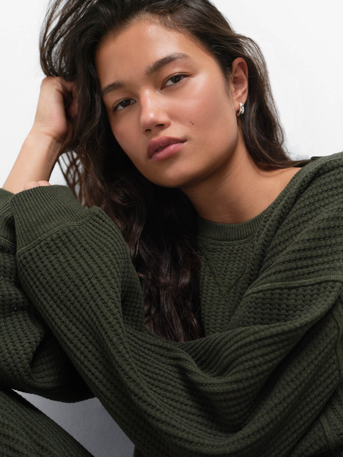 Close-up of model resting her head on her hand, wearing the Organic Waffle Crewneck Sweatshirt in Heather Pine