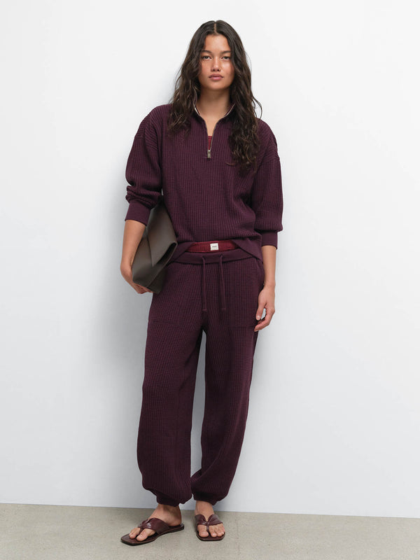 Full-length view of model with a brown shoulder bag wearing the Organic Waffle Collared Half-Zip and Sweatpant in Merlot