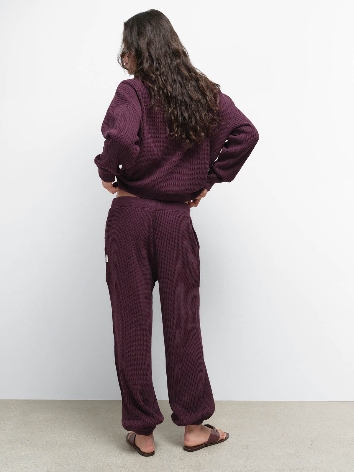 Back view of model with hands on hips wearing the Organic Waffle Collared Half-Zip and Sweatpant in Merlot