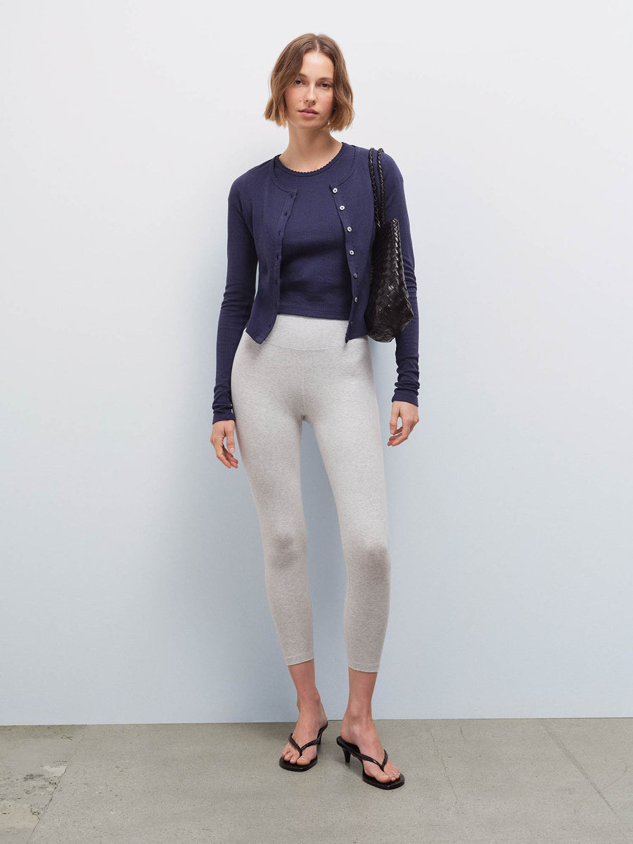 Full-length front view of a woman wearing a navy pointelle cardigan and heather grey leggings, carrying a black bag