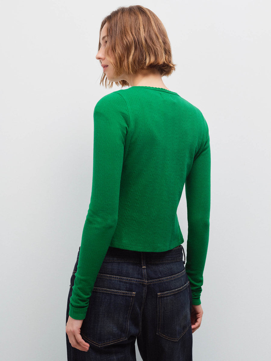 Woman wearing a green pointelle cardigan and dark denim jeans, back view in studio