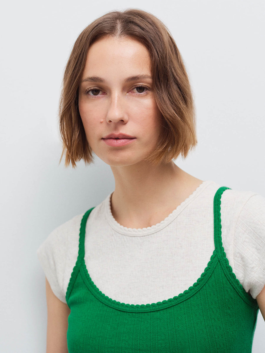 Close-up of a woman's face and shoulders wearing a green pointelle camisole layered over a cream tee