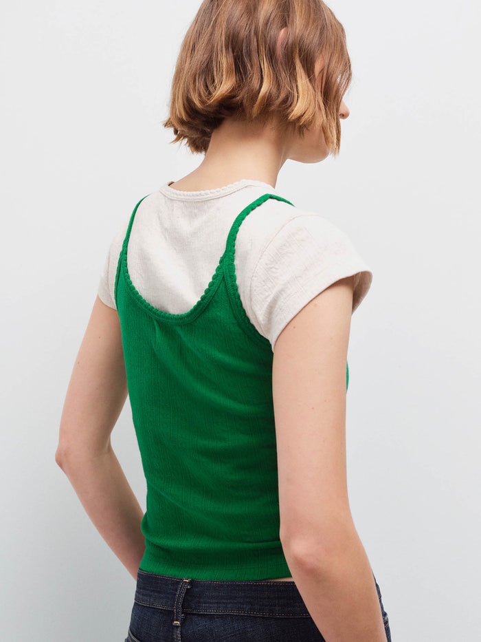 Woman standing wearing a green pointelle camisole layered over a cream tee, back view with dark denim jeans