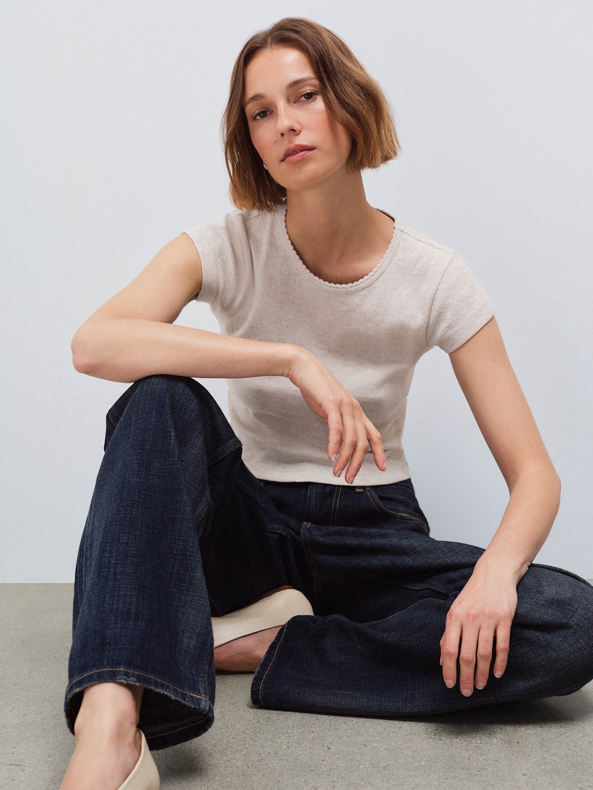 Woman seated wearing a cream cap-sleeve baby tee and dark denim jeans