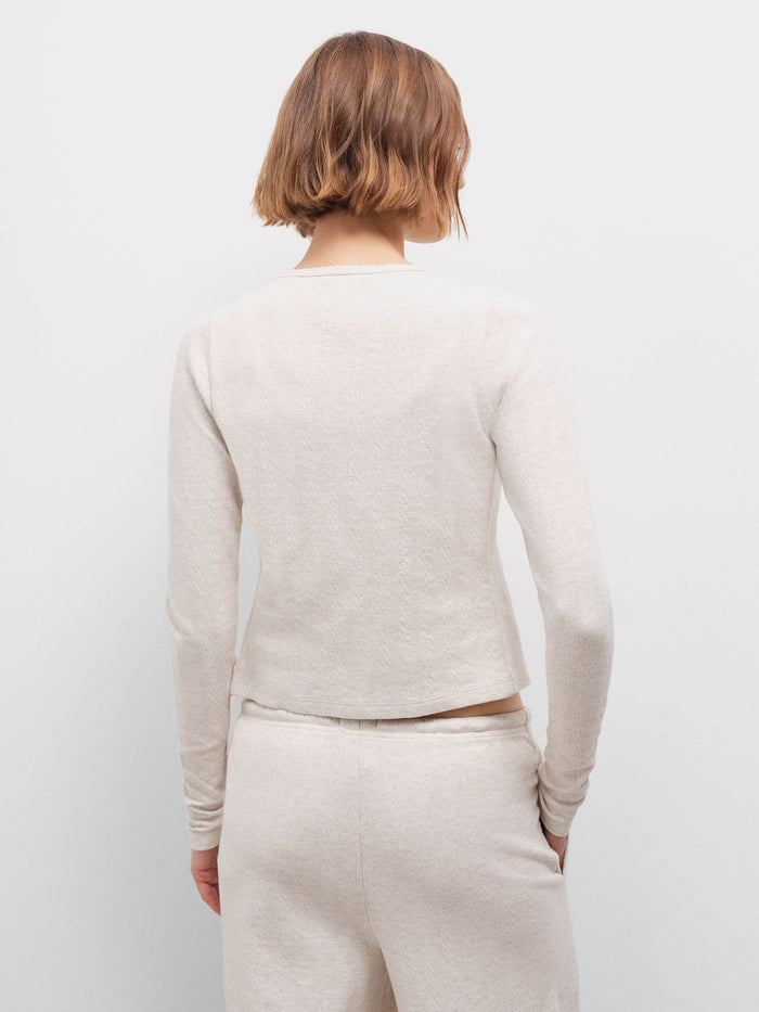 Woman wearing cream pointelle cardigan, back view showing cropped fit and ribbed texture in studio