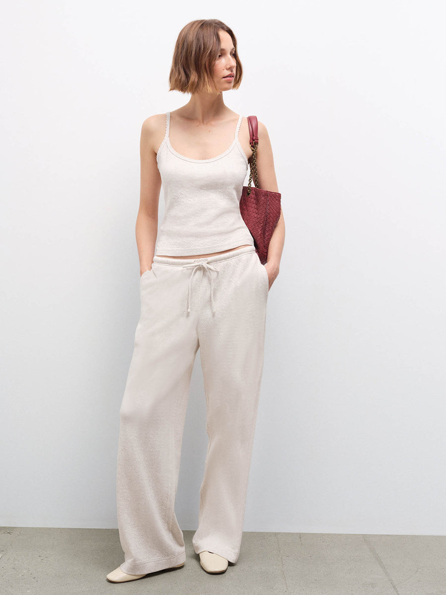 Full-body front view of a woman wearing an oatmeal ribbed camisole and wide-leg pants, carrying a burgundy woven bag