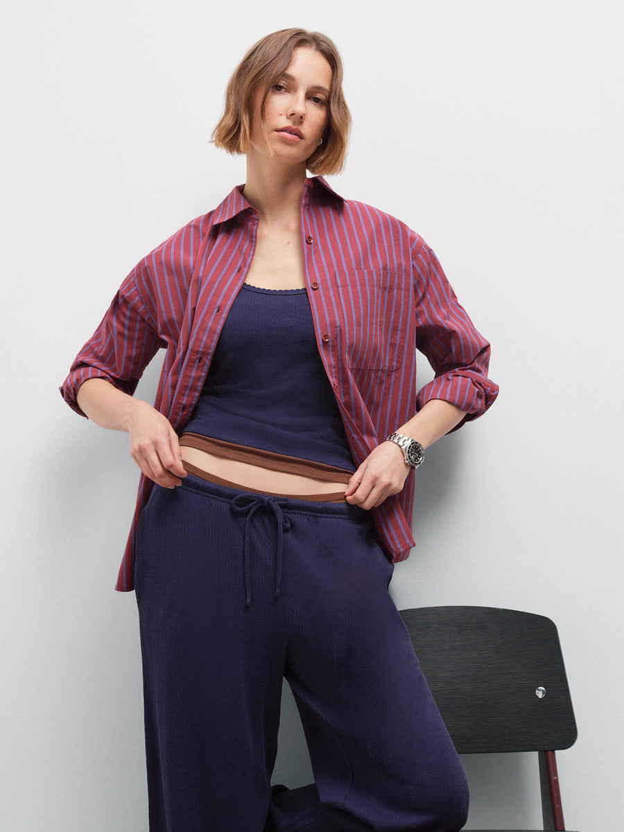 Close-up of a woman wearing a red striped open shirt over a navy tank, tucking in the waistband of matching pants