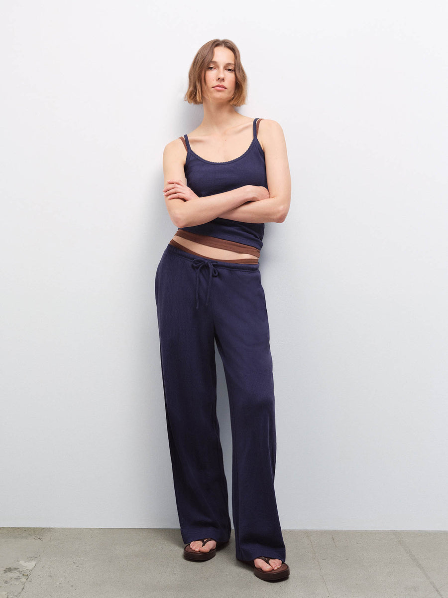 Woman with arms crossed wearing a navy pointelle tank and wide-leg pants with a sheer waistband detail