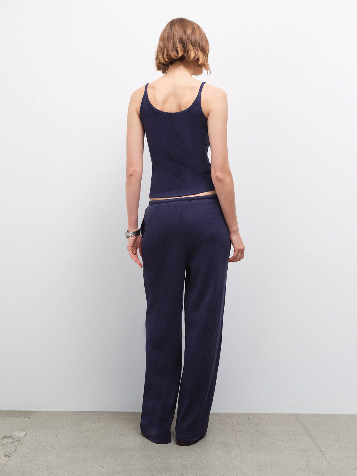 Woman standing wearing a navy pointelle tank top and matching wide-leg pants, back view in studio
