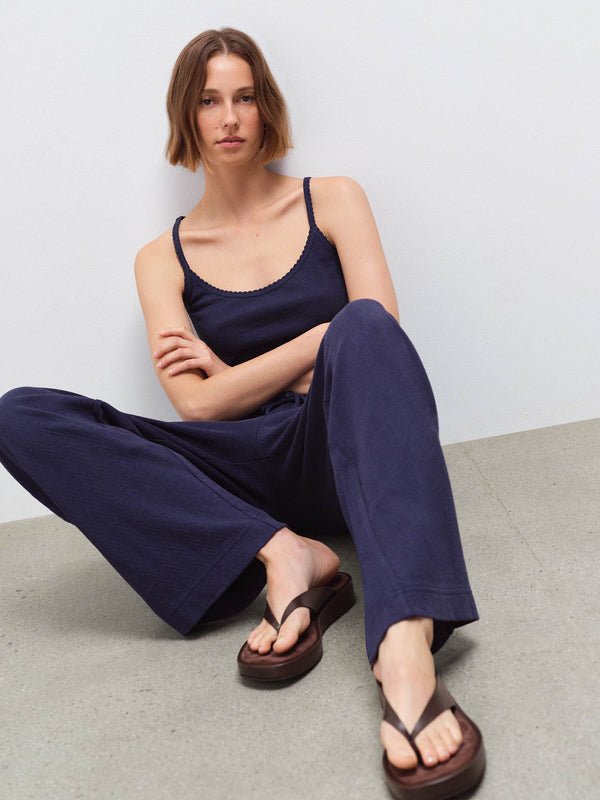 Woman seated wearing a navy pointelle scoop-neck tank top and matching wide-leg pants with brown sandals