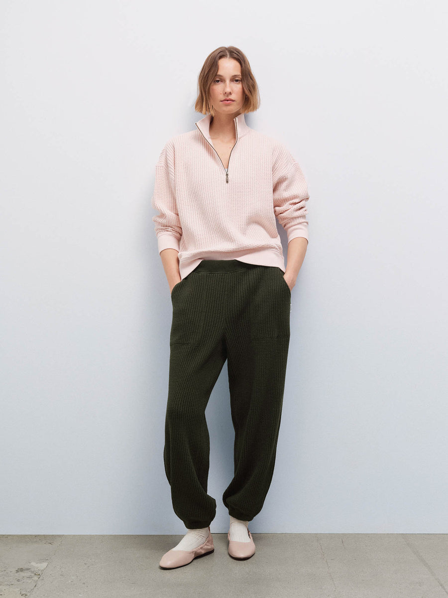 Full-length front view of a woman wearing a pale pink waffle-knit quarter-zip pullover and olive green jogger pants