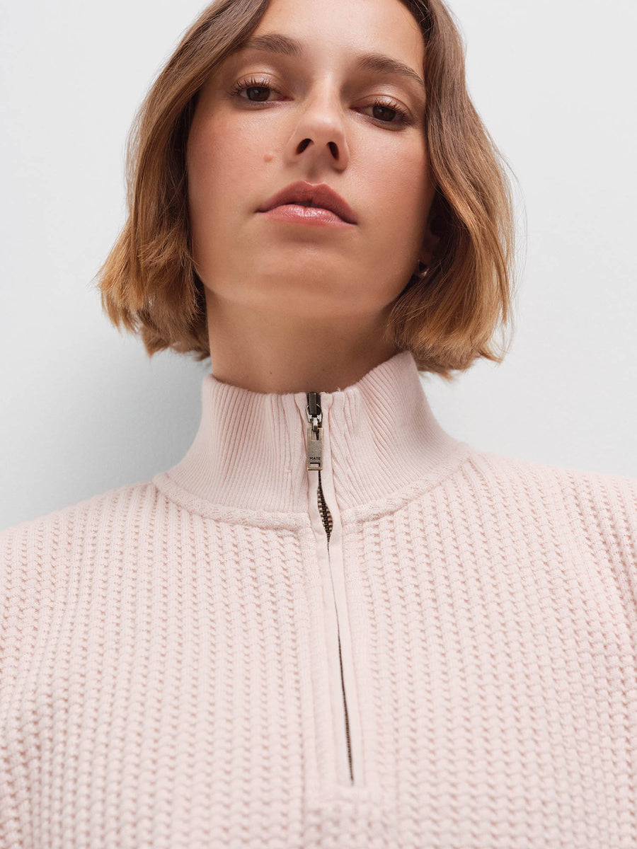 Close-up of a woman's face wearing a pale pink waffle-knit quarter-zip pullover