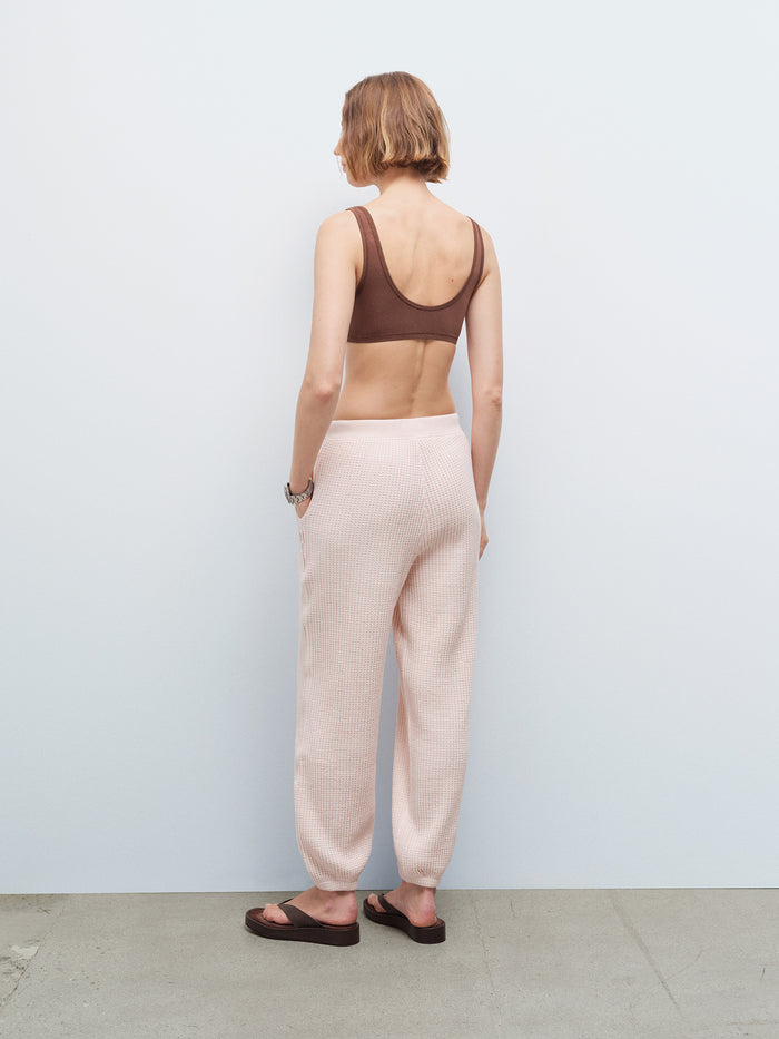 Woman wearing a brown bralette and pale pink waffle-knit jogger sweatpants, back view in studio