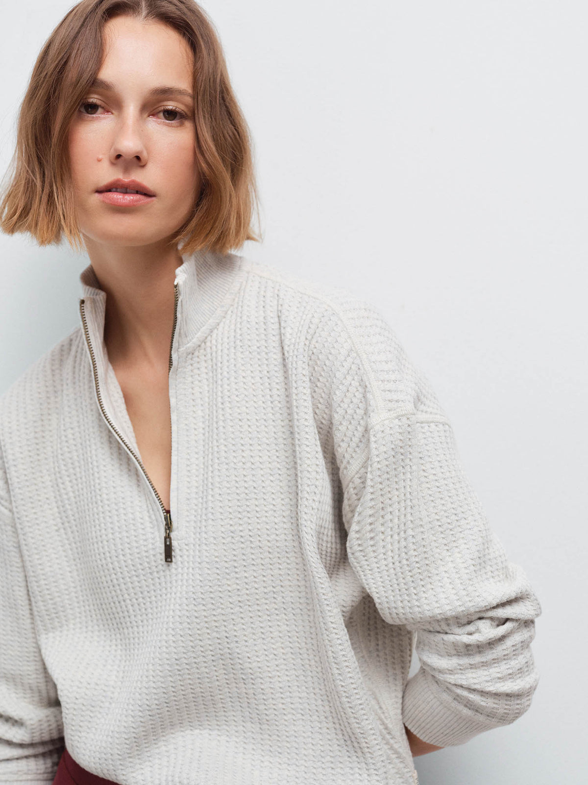 Close-up of a woman wearing a cream waffle-knit quarter-zip pullover