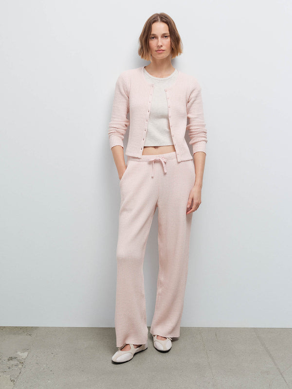 Full-length front view of a woman wearing a pale pink waffle-knit cardigan and matching wide-leg pants with white flats