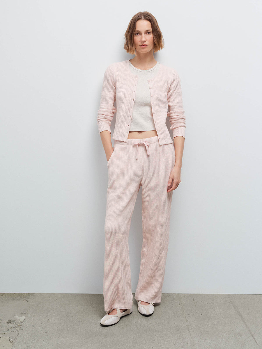 Full-length front view of a woman wearing a pale pink waffle-knit cardigan and matching wide-leg pants with white flats