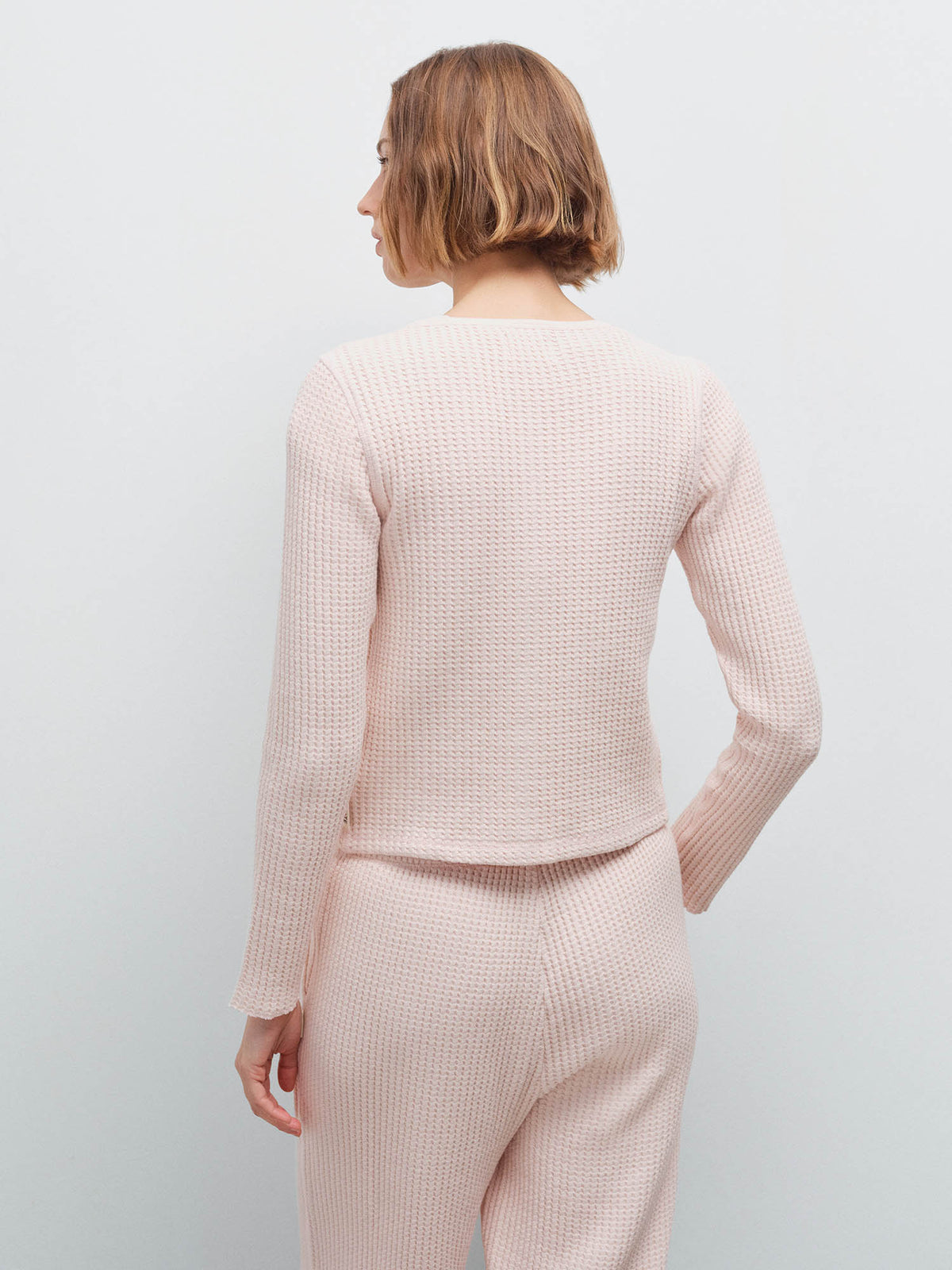 Woman wearing a pale pink waffle-knit cardigan and matching wide-leg pants, back view in studio