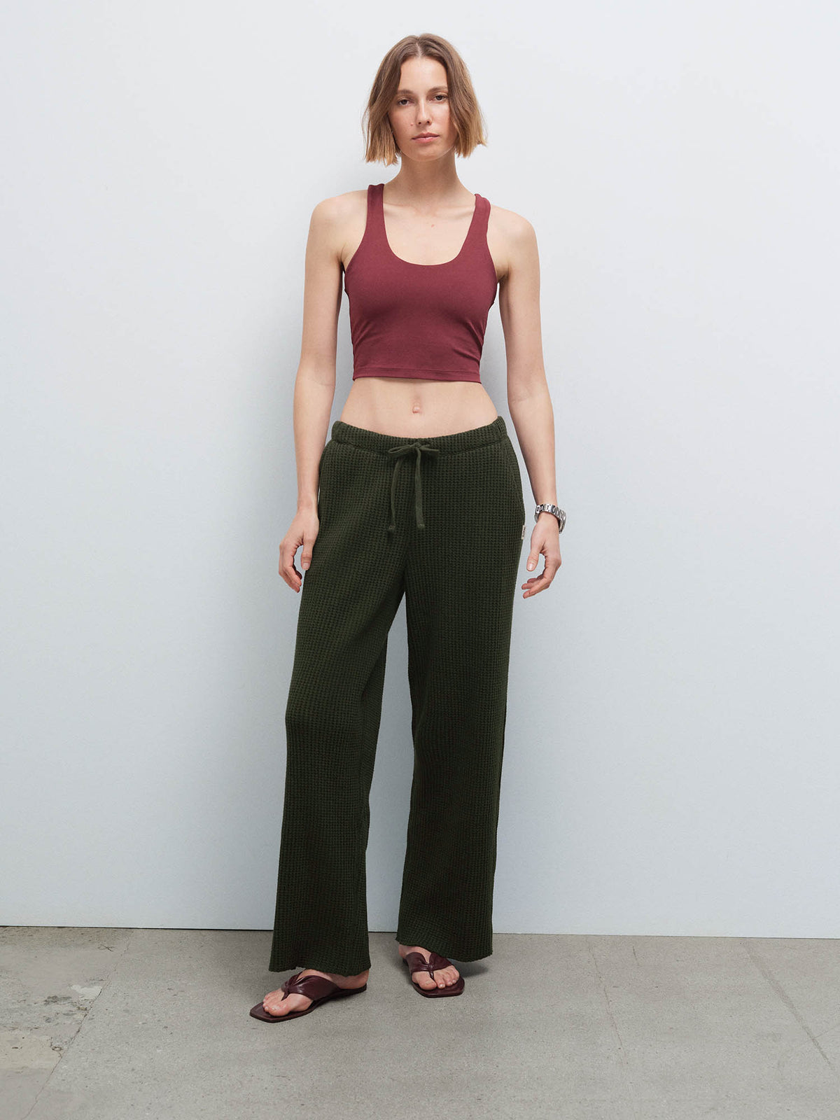 Full-length front view of a woman wearing a burgundy racerback tank and olive green waffle-knit pants with sandals