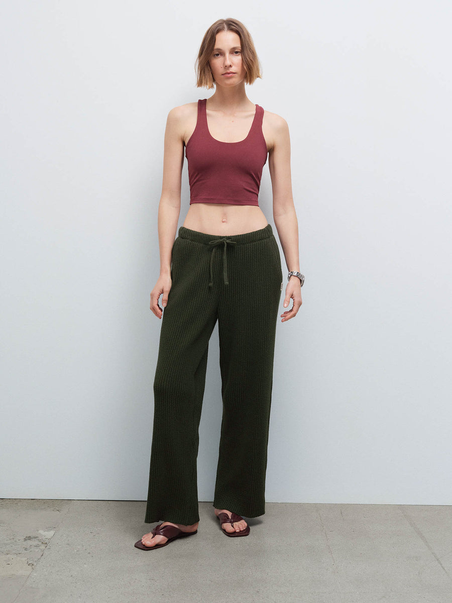 Full-length front view of a woman wearing a burgundy racerback tank and olive green waffle-knit pants with sandals