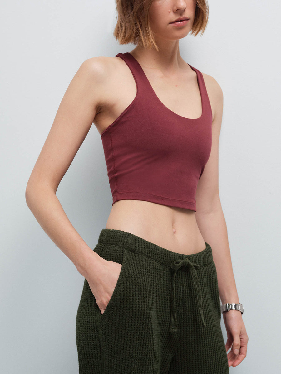 Close-up of a woman's torso wearing a burgundy racerback tank and olive green waffle-knit pants, hand in pocket