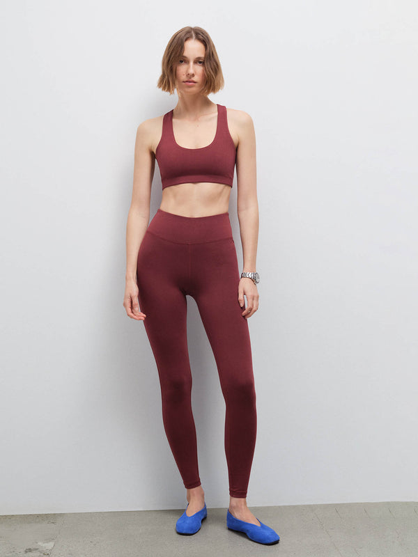 Full-length front view of a woman wearing a burgundy racerback sports bra and matching leggings with blue flats
