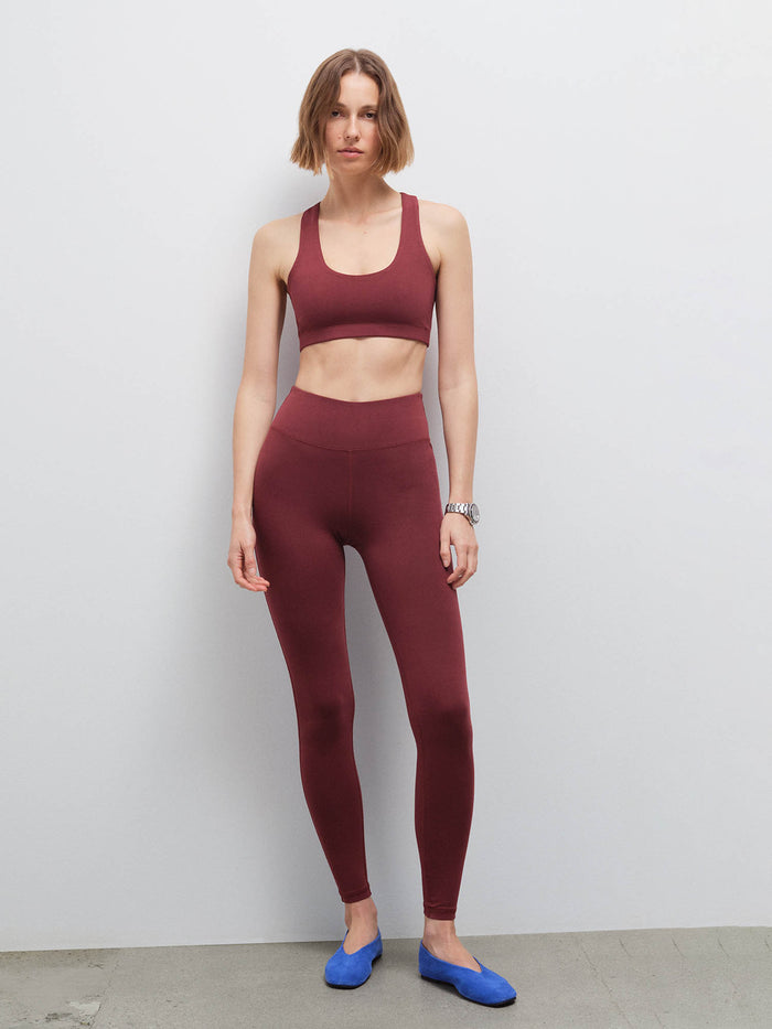 Full-length front view of a woman wearing a burgundy racerback sports bra and matching leggings with blue flats
