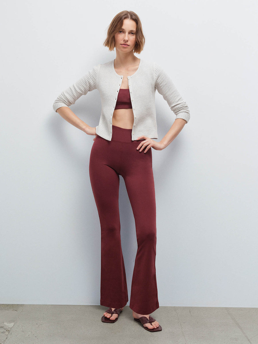 Full-length front view of a woman wearing an open cream cardigan over a burgundy scoop-neck bra and flared pants