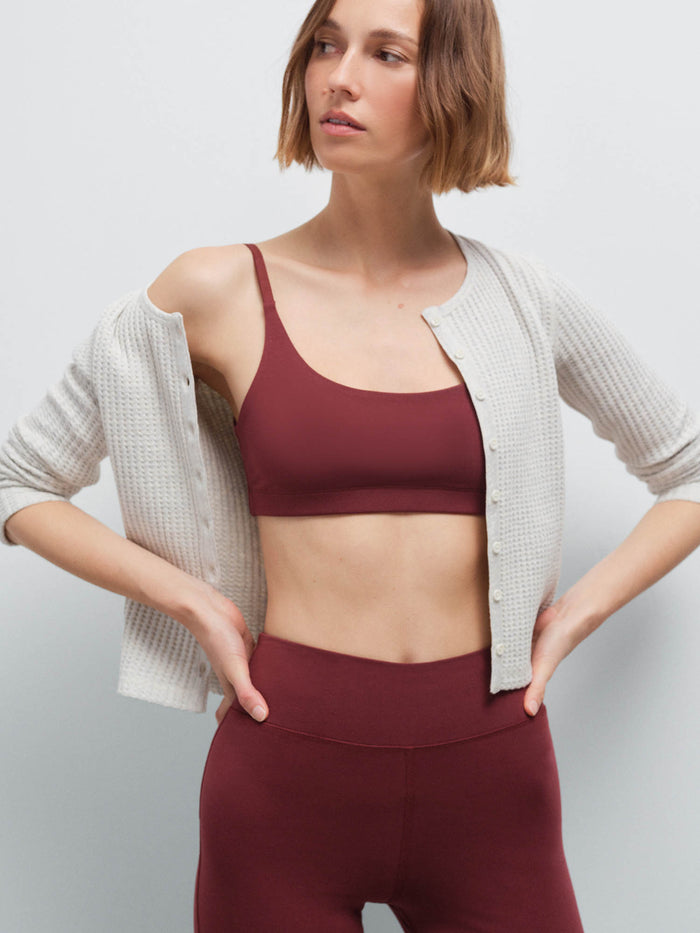 Close-up of a woman wearing an open cream waffle-knit cardigan over a burgundy scoop-neck bra and matching pants