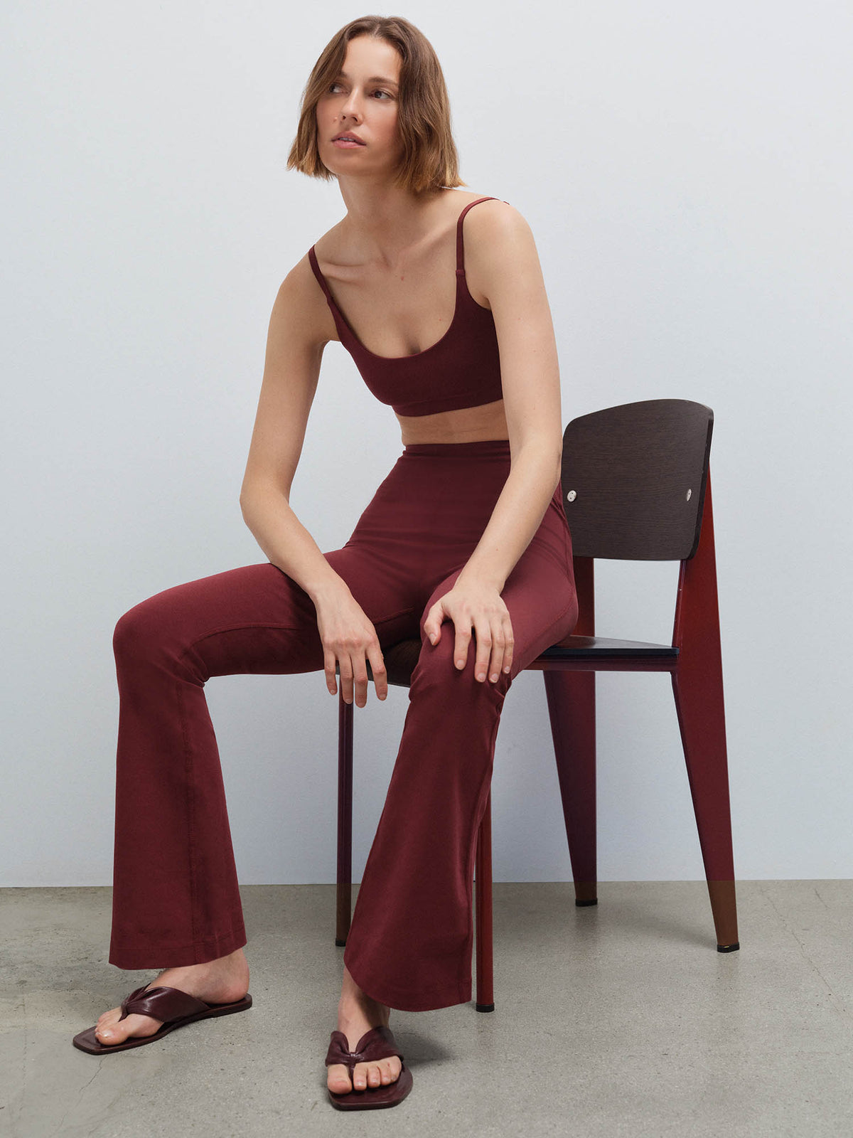 Woman seated in a chair wearing a burgundy scoop-neck bra and matching flared pants with strappy sandals