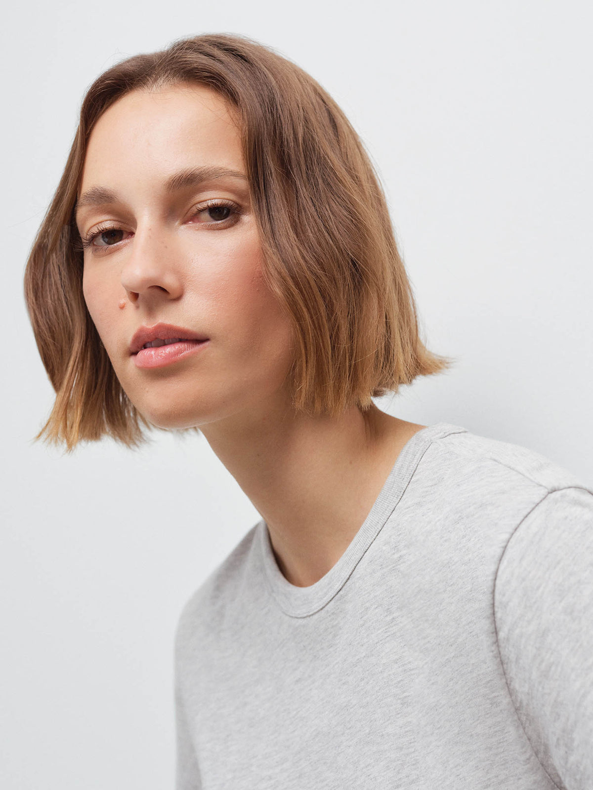 Close-up of a woman's face and shoulder wearing a heather grey crew-neck tee, tilted pose