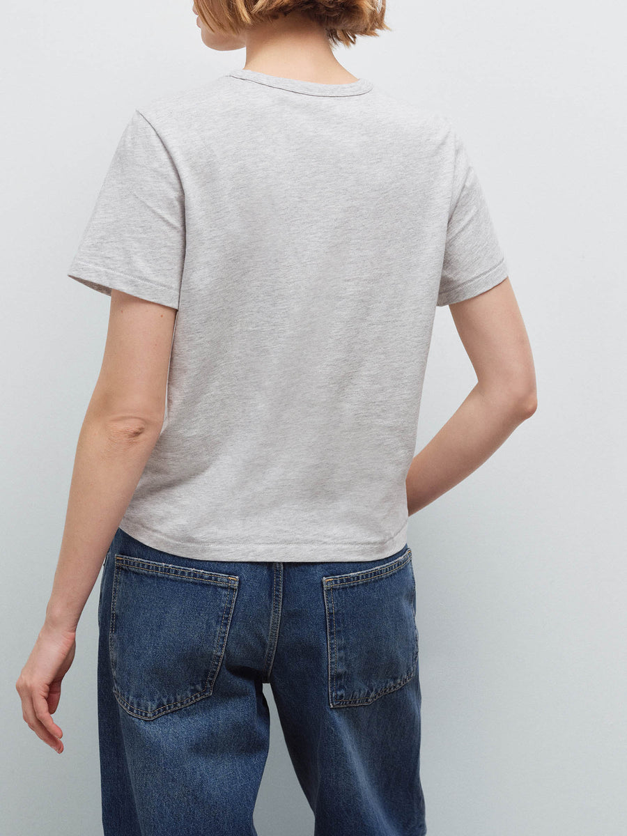 Woman wearing a heather grey crew-neck tee, back view with dark denim jeans in studio