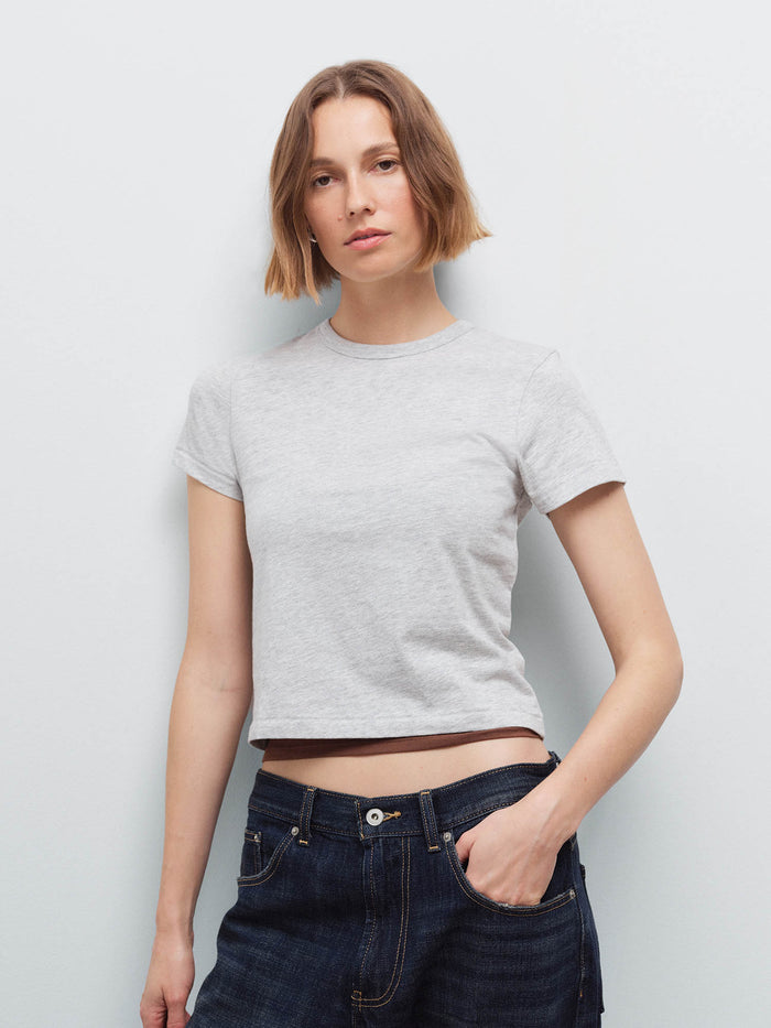 Woman wearing a light heather gray cropped crew-neck tee with dark denim jeans, front view in studio