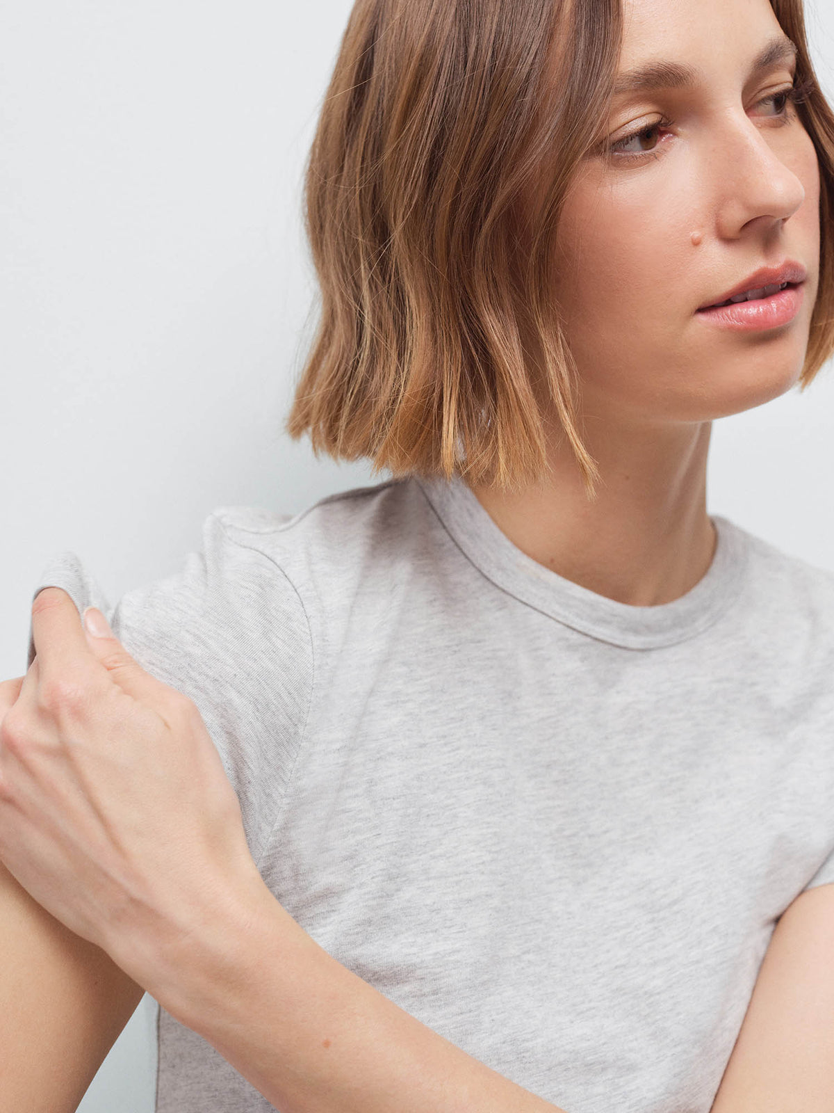 Close-up of a woman's face and shoulder wearing a light heather gray cropped crew-neck tee, studio