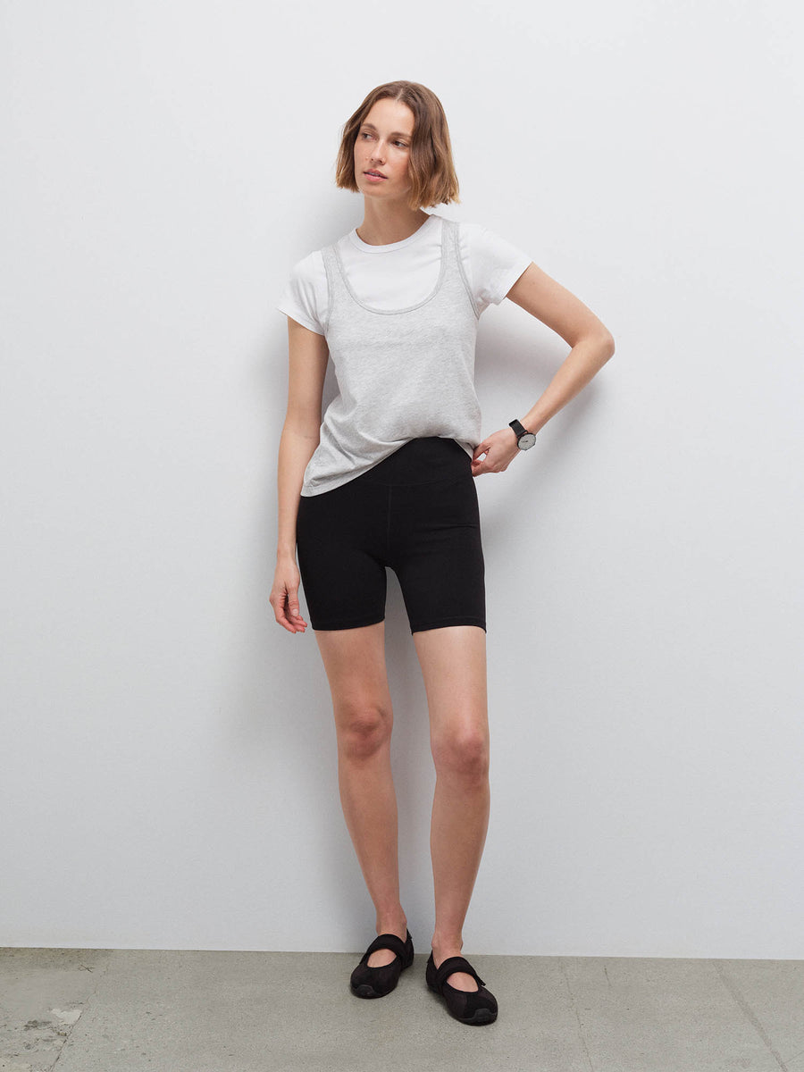 Full-length front view of a woman wearing a heather grey tank layered over a white tee with black biker shorts