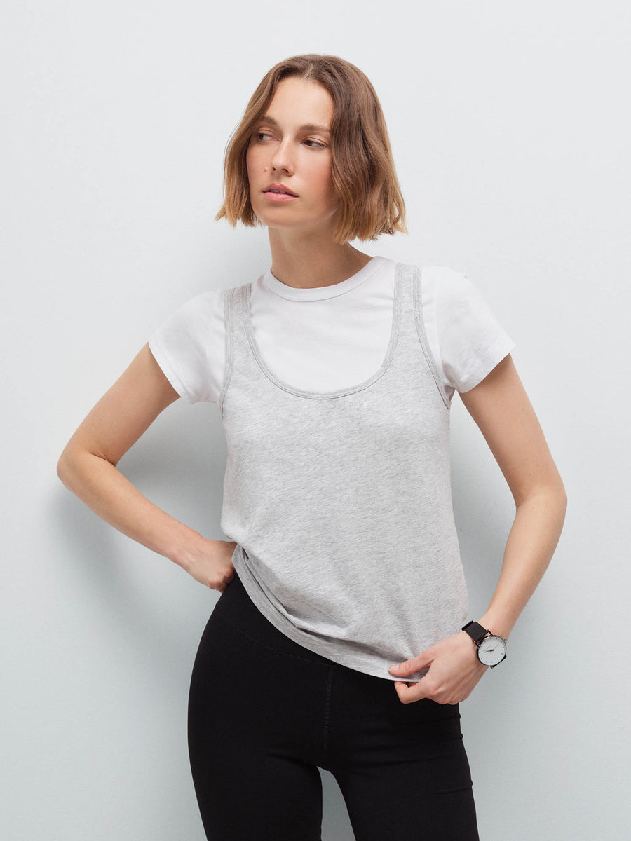 Woman wearing a heather grey tank layered over a white tee with black leggings, hand on hip
