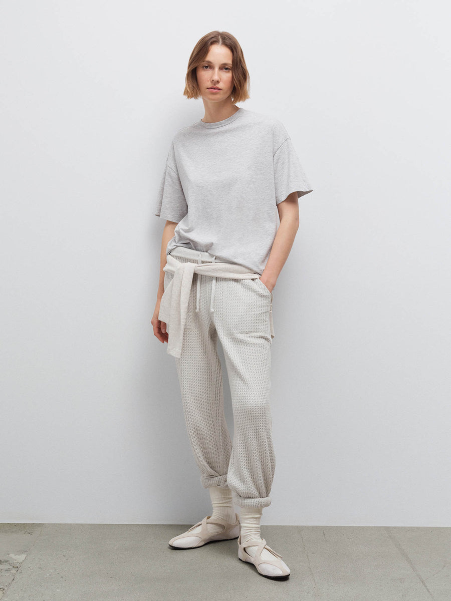Woman wearing heather grey oversized pima tee and cream sweatpants with a sweater tied at waist, studio