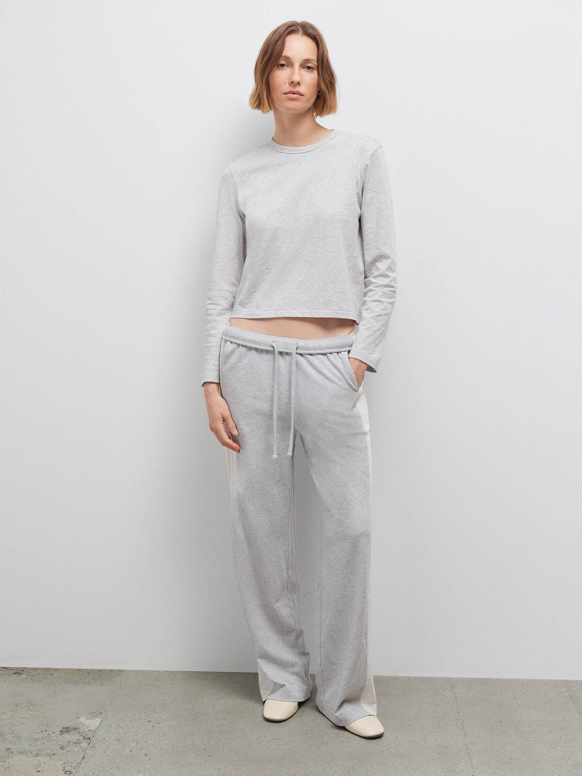 Full-length front view of a woman wearing a heather grey long-sleeve top and wide-leg sweatpants with cream flats