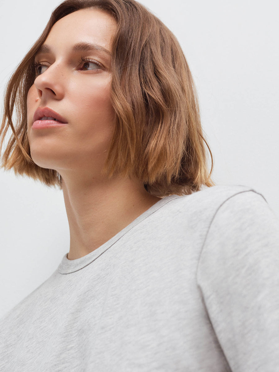 Close-up side profile of a woman's face and shoulder wearing a heather grey long-sleeve top