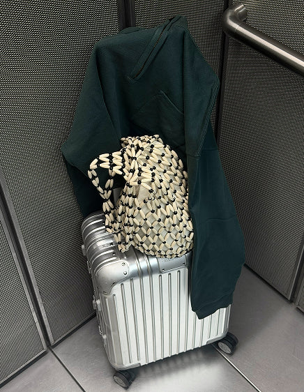 Dark green organic sweatshirt over a silver carry-on with a woven tote – MATE the Label travel edit